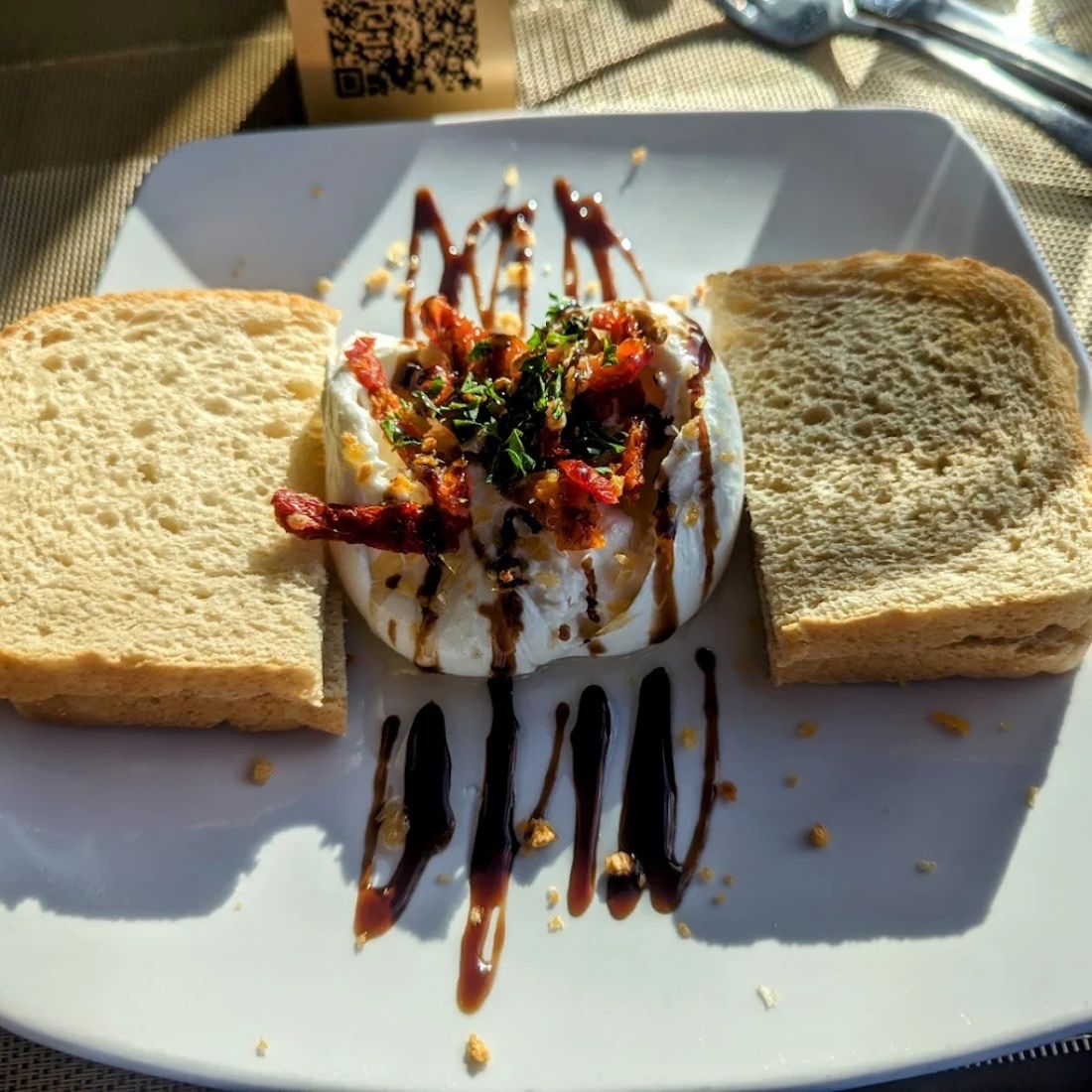 A round of burrata under a balsamic drizzle and sun dried tomatoes, plated between two thick slices of toast.
