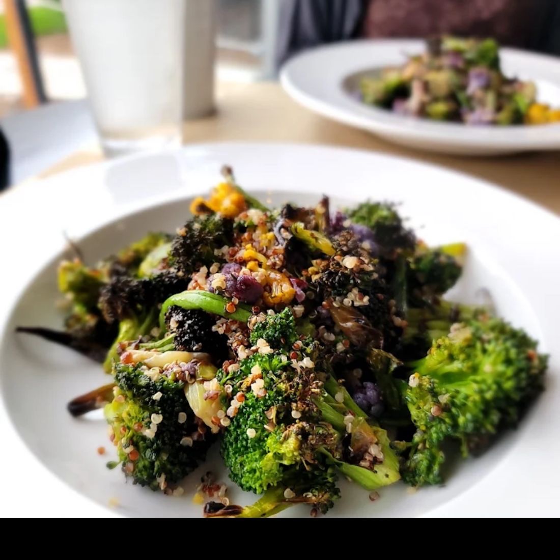A bowl of charred broccoli tossed with quinoa and roasted purple cauliflower, on a table by a window.