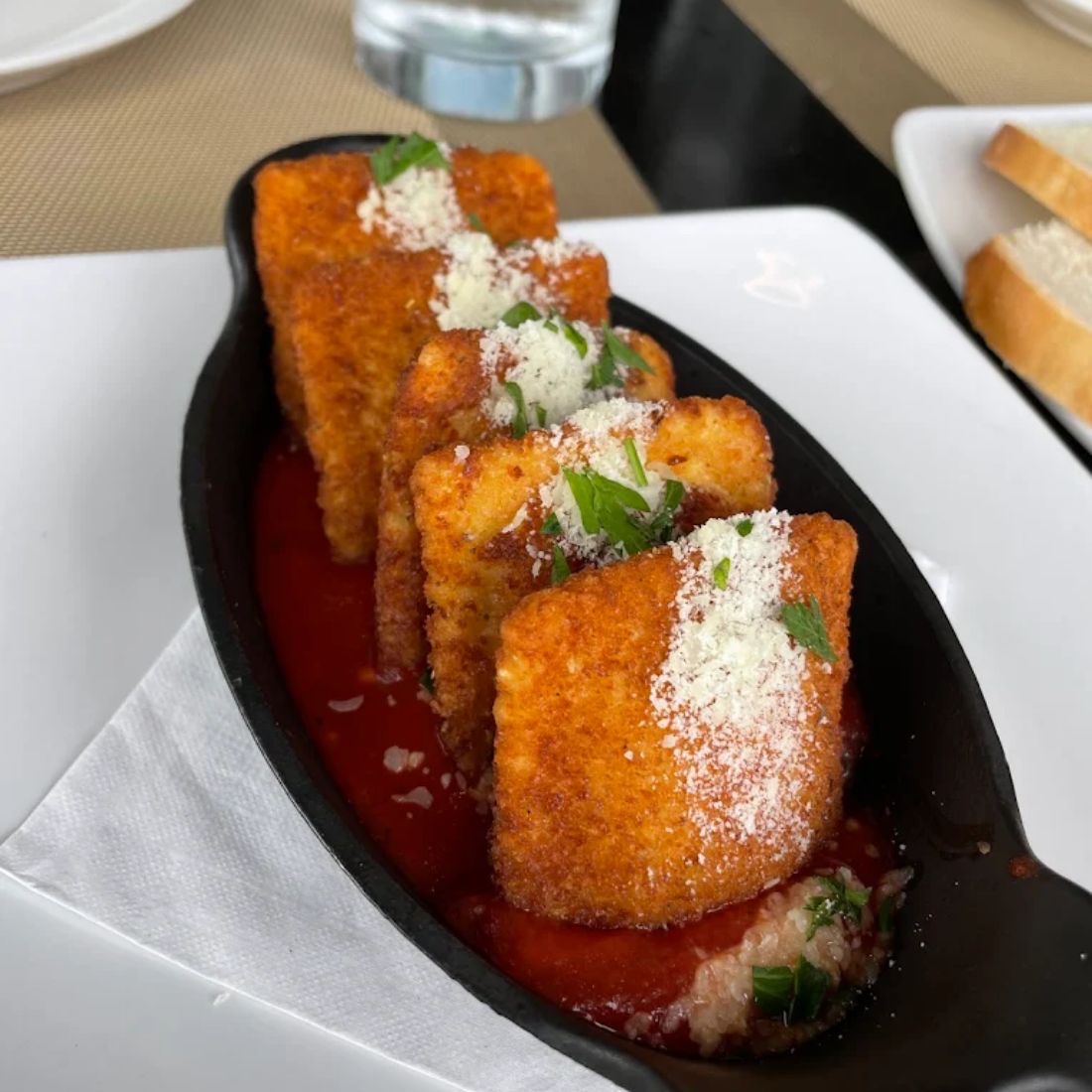 Five breaded ravioli standing in a cast iron dish of marinara, dusted with parmesan and parsley.